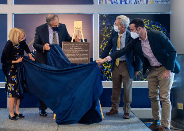 President Emerita Mary Sue Coleman, President Mark Schlissel, LSI Director Roger Cone and Board of Regents Chair Jordan Acker unveil the replica of a plaque that will be installed on the newly named Mary Sue Coleman Hall.