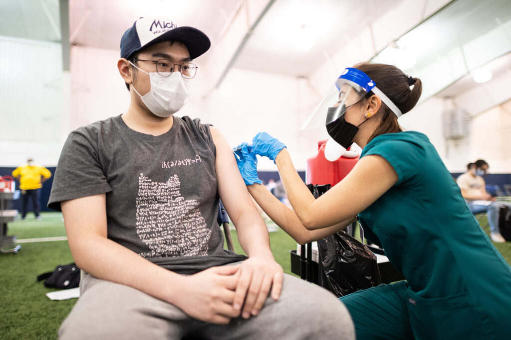 A student gets a vaccine from a pharmacy student at a University of Michigan clinic in the athletics training facility.